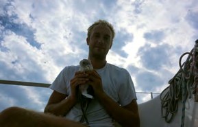 Simon hält einen Vogel in den Händen, dahinter Wolken
