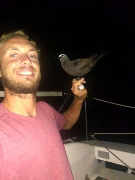 Simon mit einem Vogel auf der Hand, nachts an Deck
