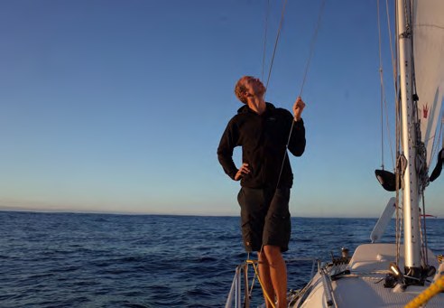 Simon steht am Bug des Segelboots und blickt aufs Meer