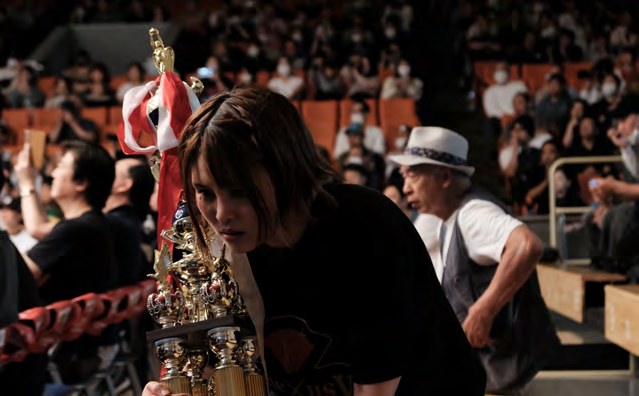 Die Wrestlerin Thekla mit Pokal zwischen Zuschauerinnen und Zuschauern in Tokio.