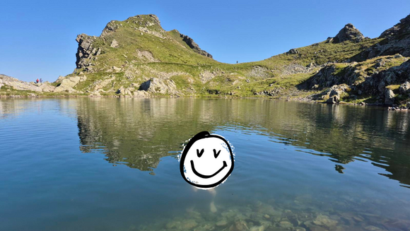 Ein Gebirgssee, in dessen Wasserfläche ein gezeichneter Smiley liegt