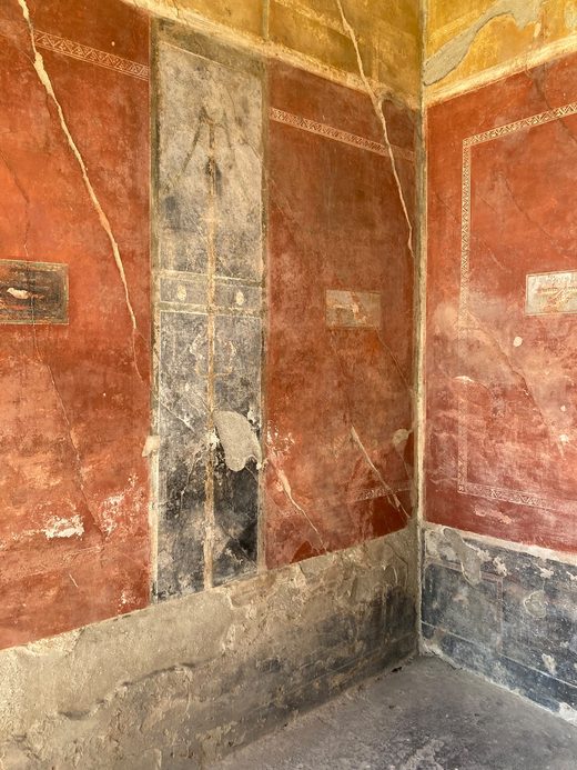 Rot bemalter Wohnraum in Pompeji mit kleinen gemalten Bildtafeln