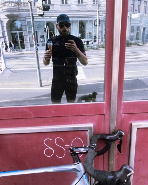 Andreas im Radtrikot, Selfie in einer Glastür, mit Eis in der Hand und dem Rennrad davor