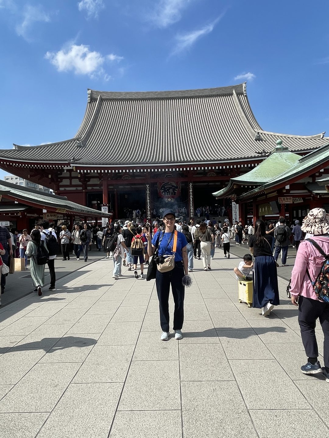 Iris steht lächelnd vor einem großen Tempel in Tokio, um sie herum viele Besucher:innen
