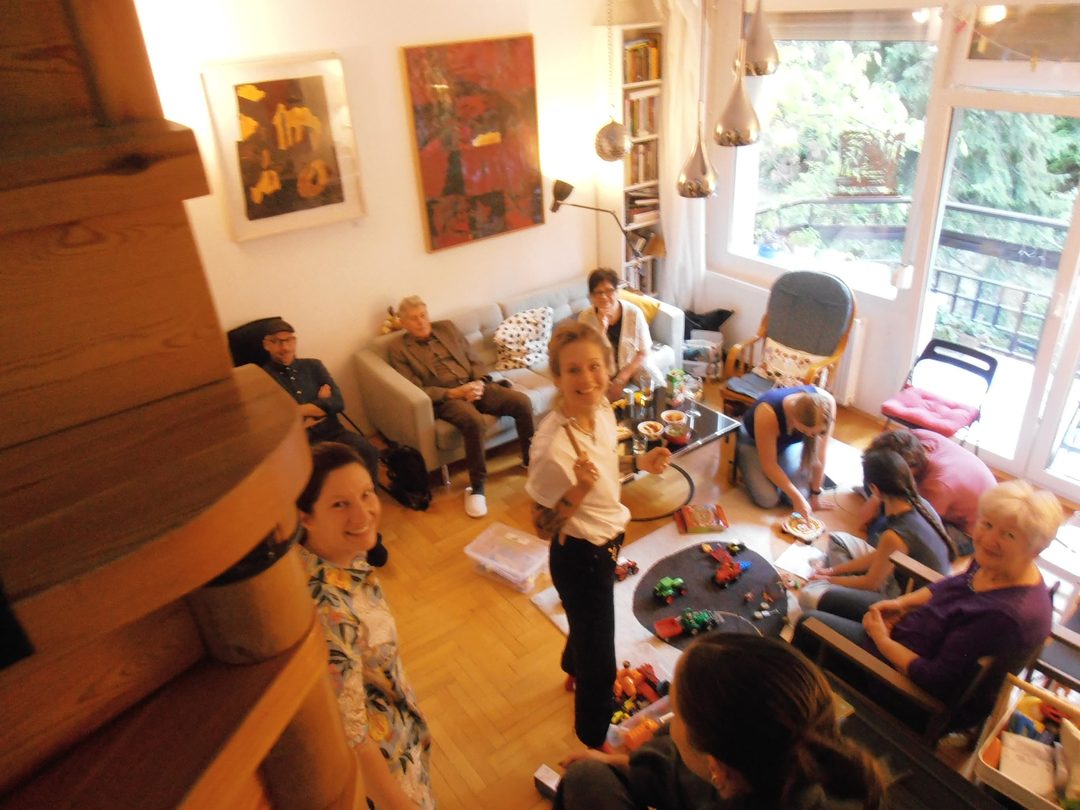 Blick von oben in ein Wohnzimmer: Eine Familie sitzt beisammen, Kinder spielen am Boden