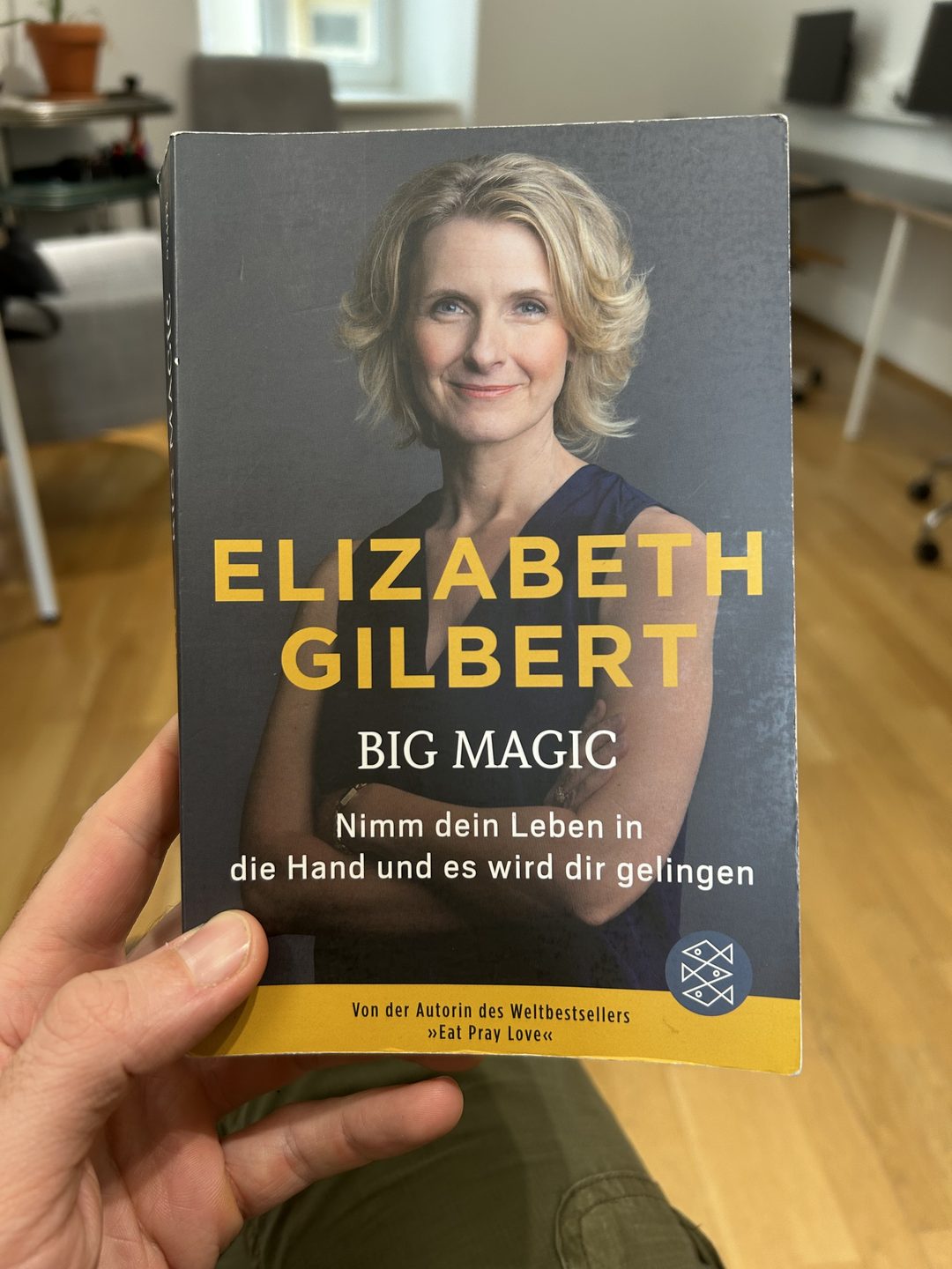 Eine Hand hält ein Taschenbuch von „Big Magic“ von Elizabeth Gilbert, auf dem Cover ein Porträt der Autorin