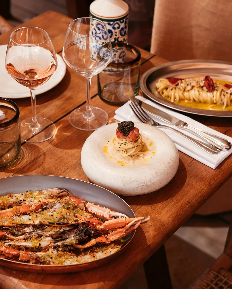 A selection of signature dishes at Casita — spaghetti topped with caviar, grilled langoustines, and pasta with fresh seafood, served with rosé wine on a wooden table.
