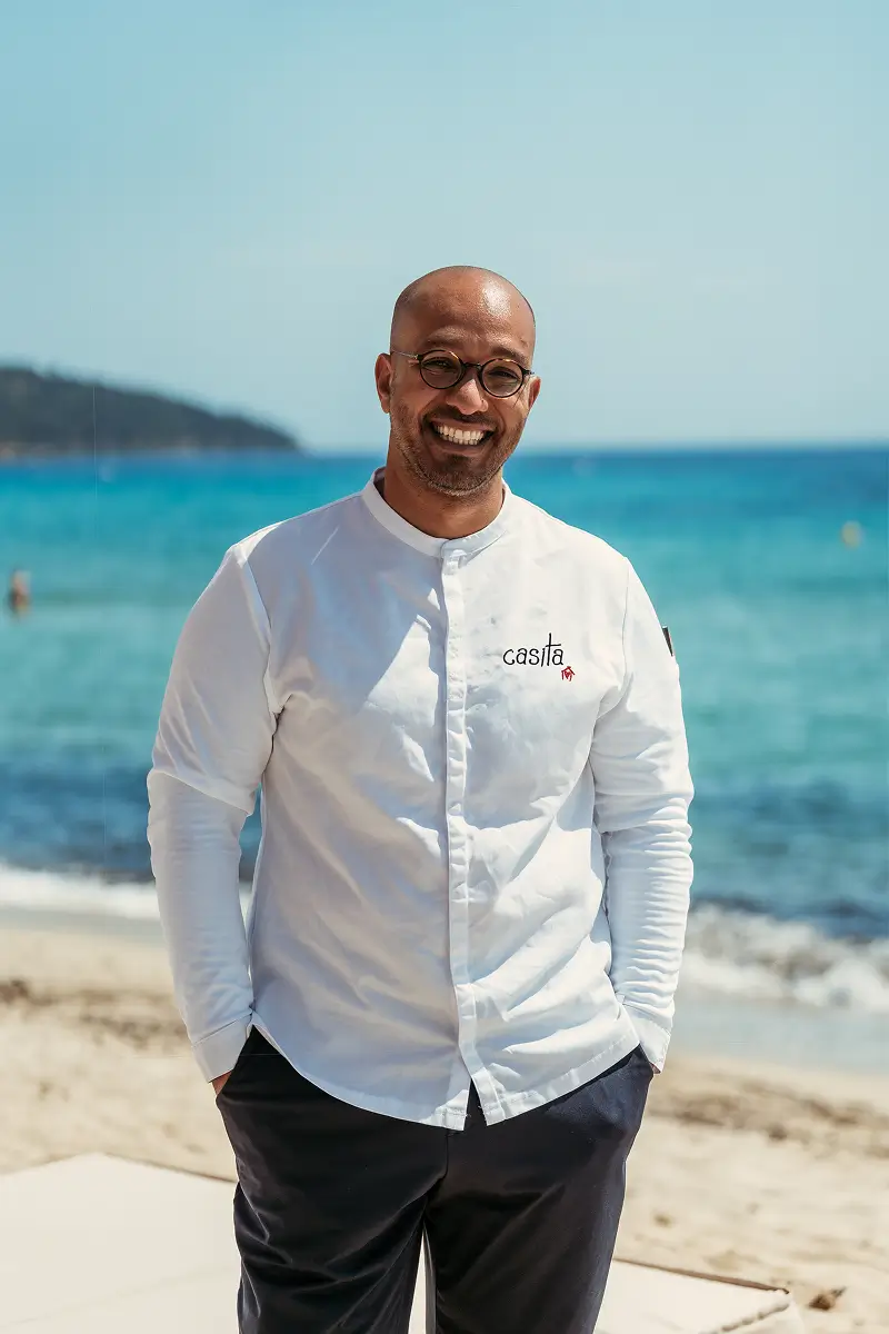Chef Zouhair smiling, wearing a Casita chef's jacket, with the sea in Saint-Tropez in the background