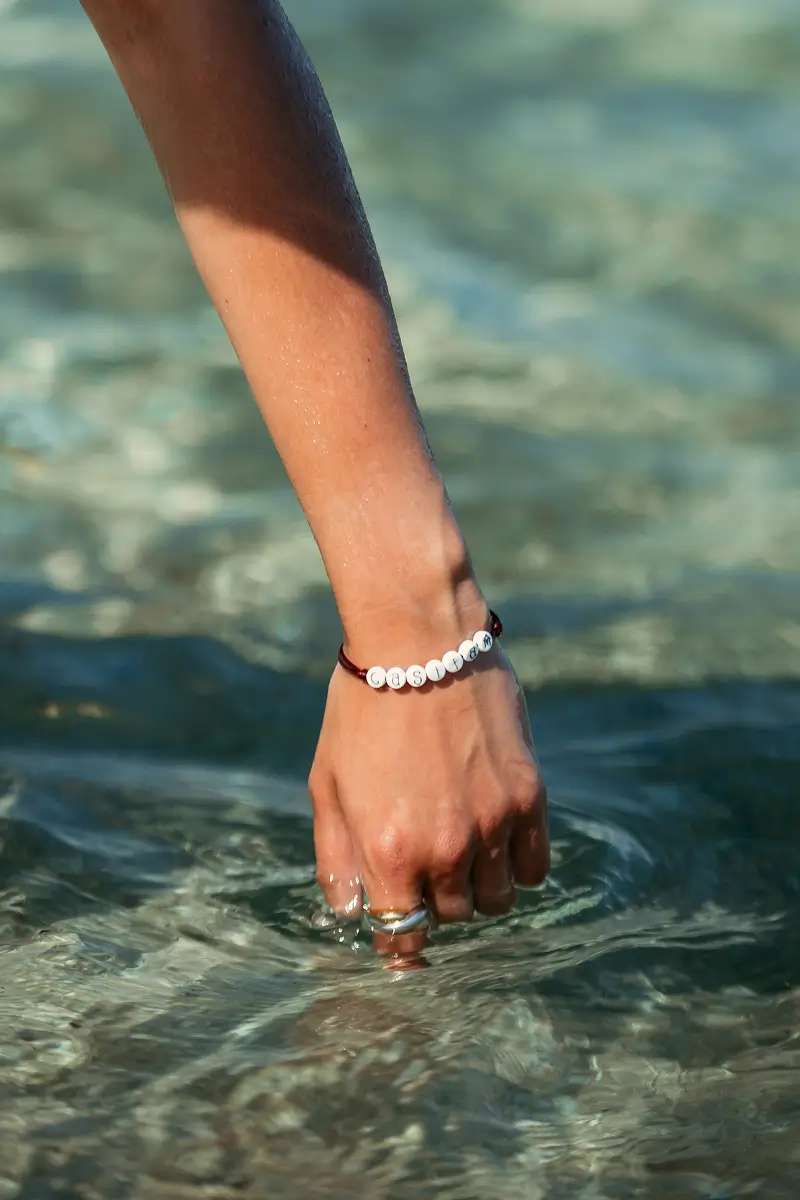 Hand with a Casita beaded bracelet dipping into clear turquoise sea water