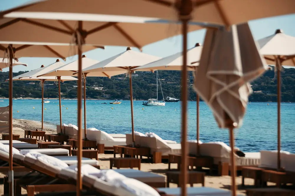 White parasols and sunbeds at Casita beach club overlooking the sea with sailboats and yachts