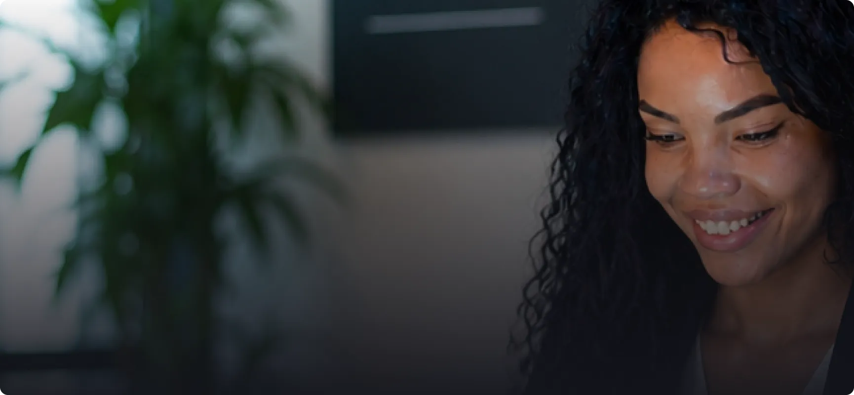 Smiling woman with curly hair looking down in a softly lit indoor setting.