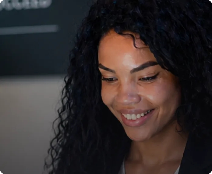 Smiling woman with curly black hair looking down in a softly lit indoor setting.