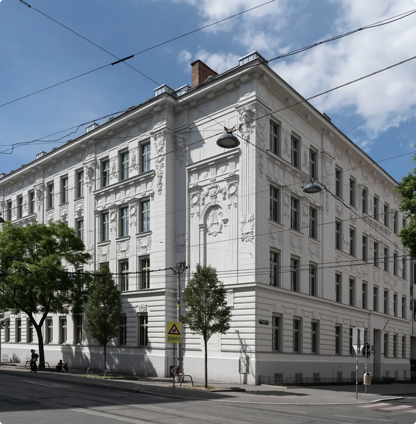 Historisches Schulgebäude mit weißen Fassaden und Verzierungen an einer Straßenkreuzung.