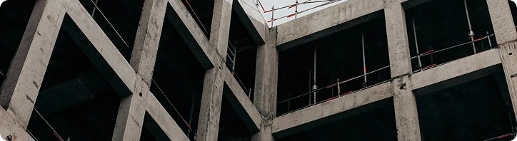Rohbau eines mehrstöckigen Gebäudes aus Beton mit Stahlgerüsten und geöffneten Fensterrahmen.