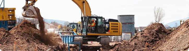 Bagger hebt Erde bei einer Baustelle mit Erdhügeln und Baugeräten im Hintergrund.