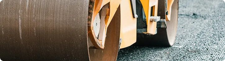 Großer Walzenverdichter auf frisch asphaltierter Straße für den Straßenbau.