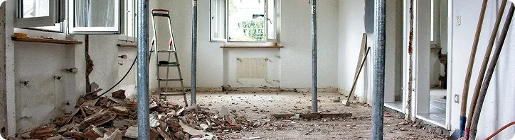 Baustelle mit Betonsäulen und Schutt auf Boden in einem Zimmer mit weißen Wänden und Fenstern.