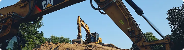 Bau bagger auf einem hügel aus erde unter klarem blauem himmel mit bäumen im hintergrund.