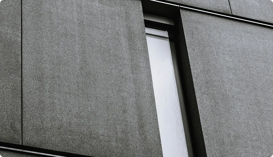 Schmale, hohe Fensteröffnung in einer grauen Betonfassade eines modernen Gebäudes.
