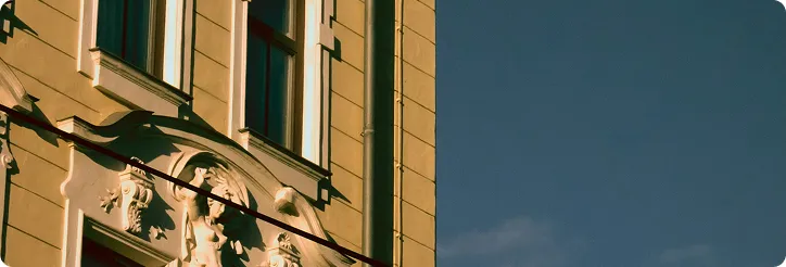 Nahaufnahme eines Gebäudes mit dekorativen Skulpturen unter Fenstern bei blauem Himmel.