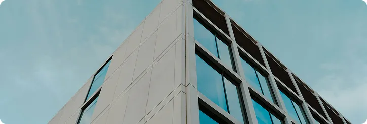 Moderne Ecke eines mehrstöckigen Bürogebäudes mit Glasfenstern vor blauem Himmel.