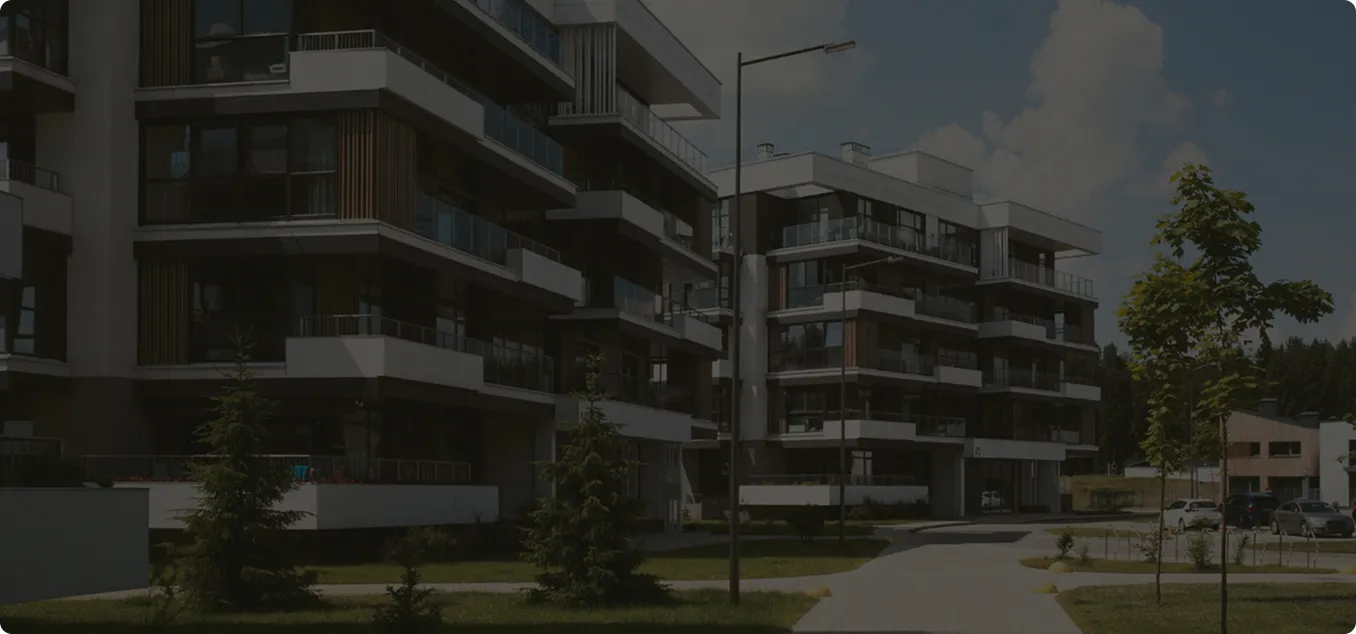 Moderne Wohnhäuser mit Balkonen, Grünflächen und Parkplätzen unter blauem Himmel.
