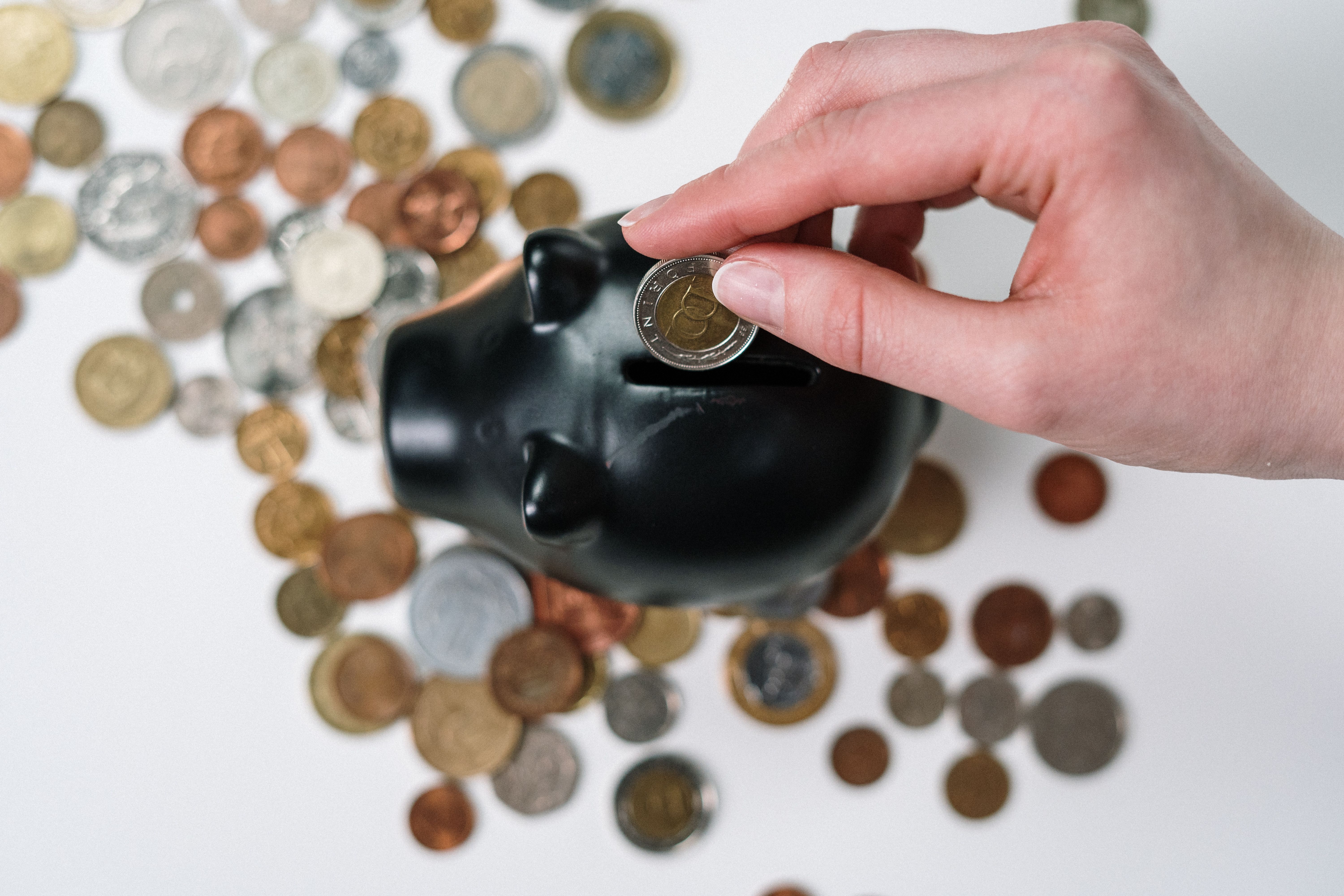 Main déposant une pièce dans une tirelire entourée de monnaie