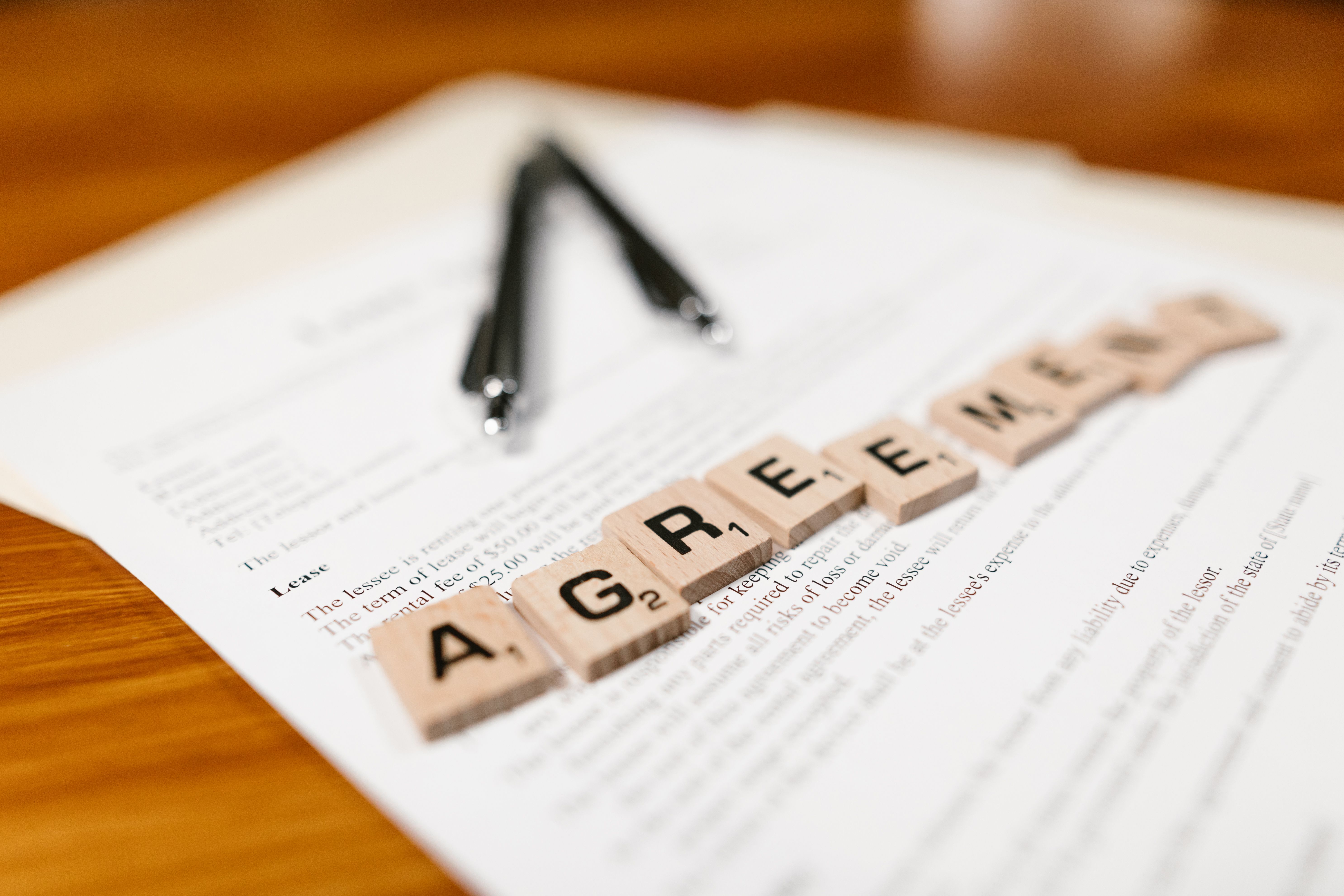 Lettres formant le mot agreement posées sur un contrat, à côté de lunettes