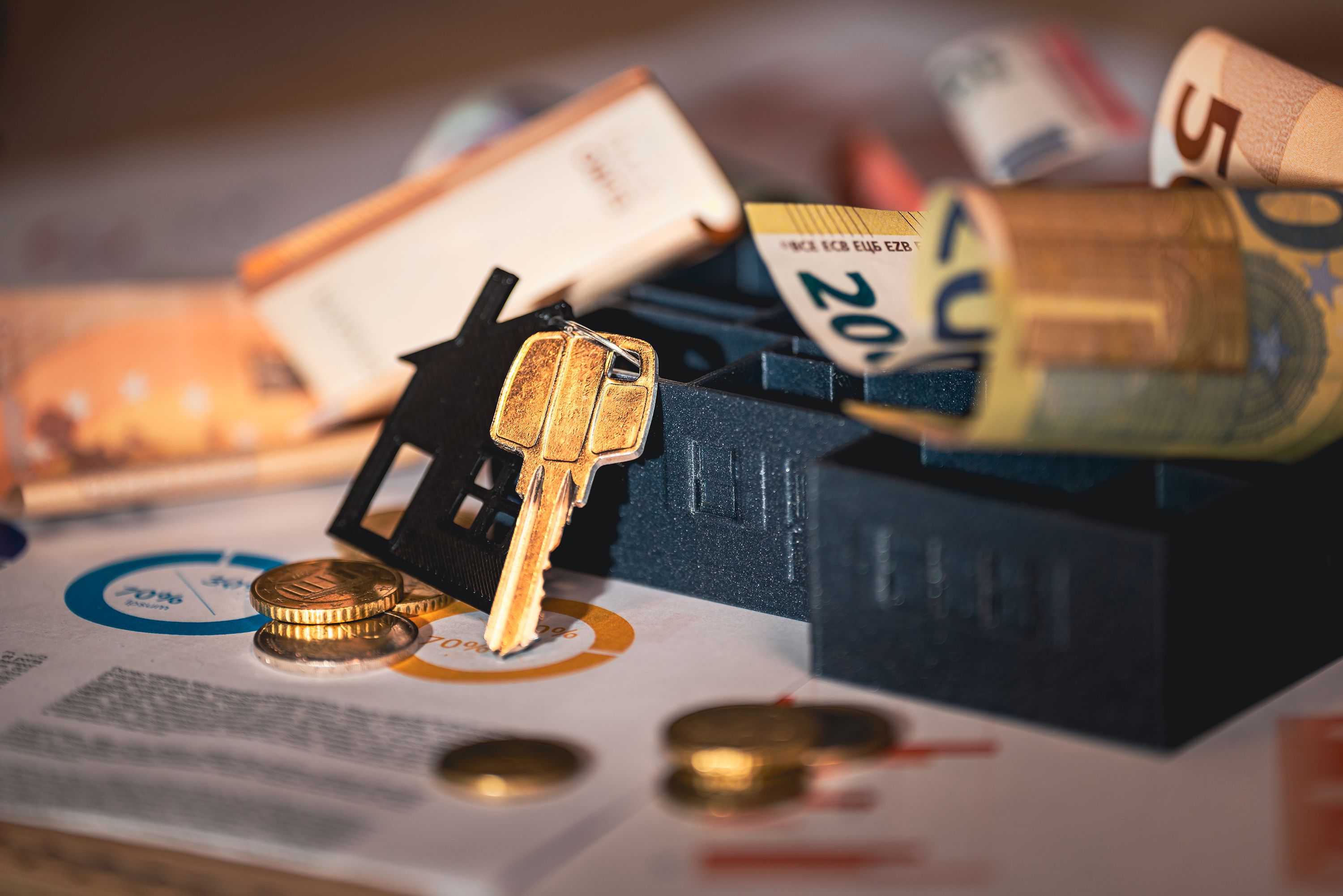 Clé de maison posée sur des billets et des pièces