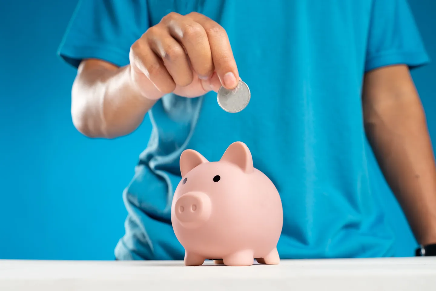 A person slipping a coin into a piggy bank