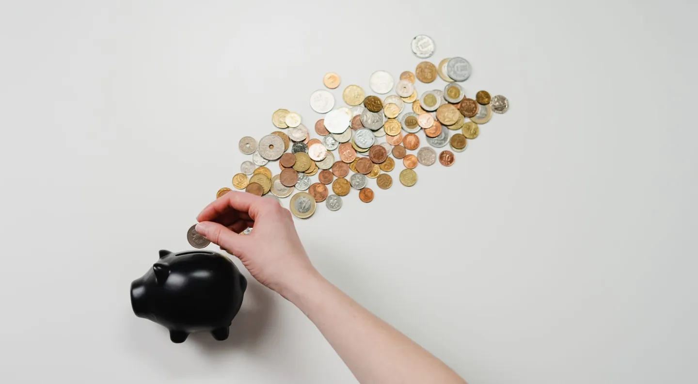 A hand sliding a shower of coins into a black piggy bank