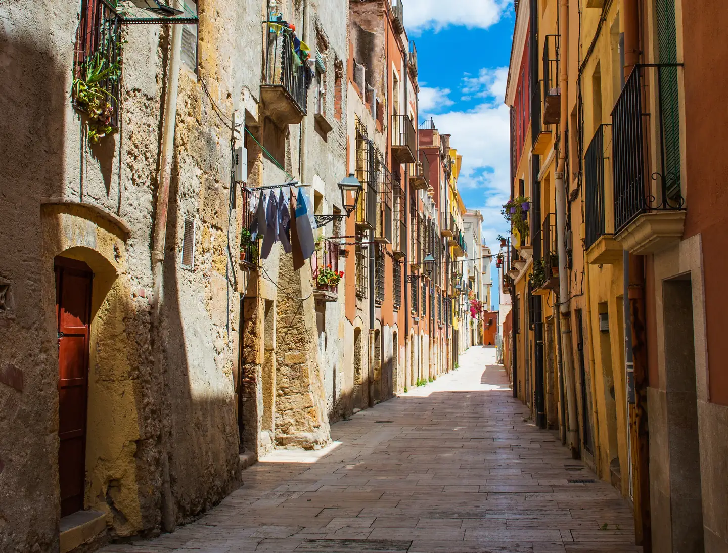 Callejuela estrecha flanqueada por fachadas de color ocre con ropa tendida en las ventanas
