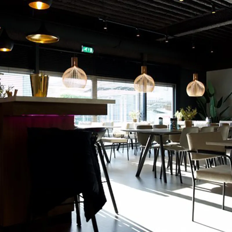 Moderne eetruimte met lichtgevende hanglampen, tafels en stoelen naast grote ramen met zonlicht.