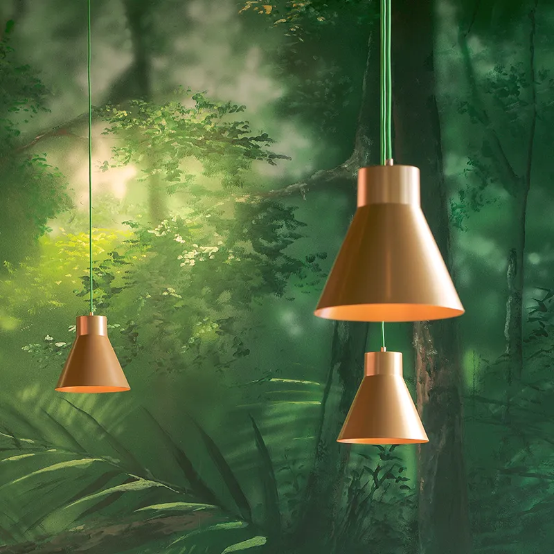 Drie koperkleurige hanglampen hangen voor een groene muur met bosmotieven.