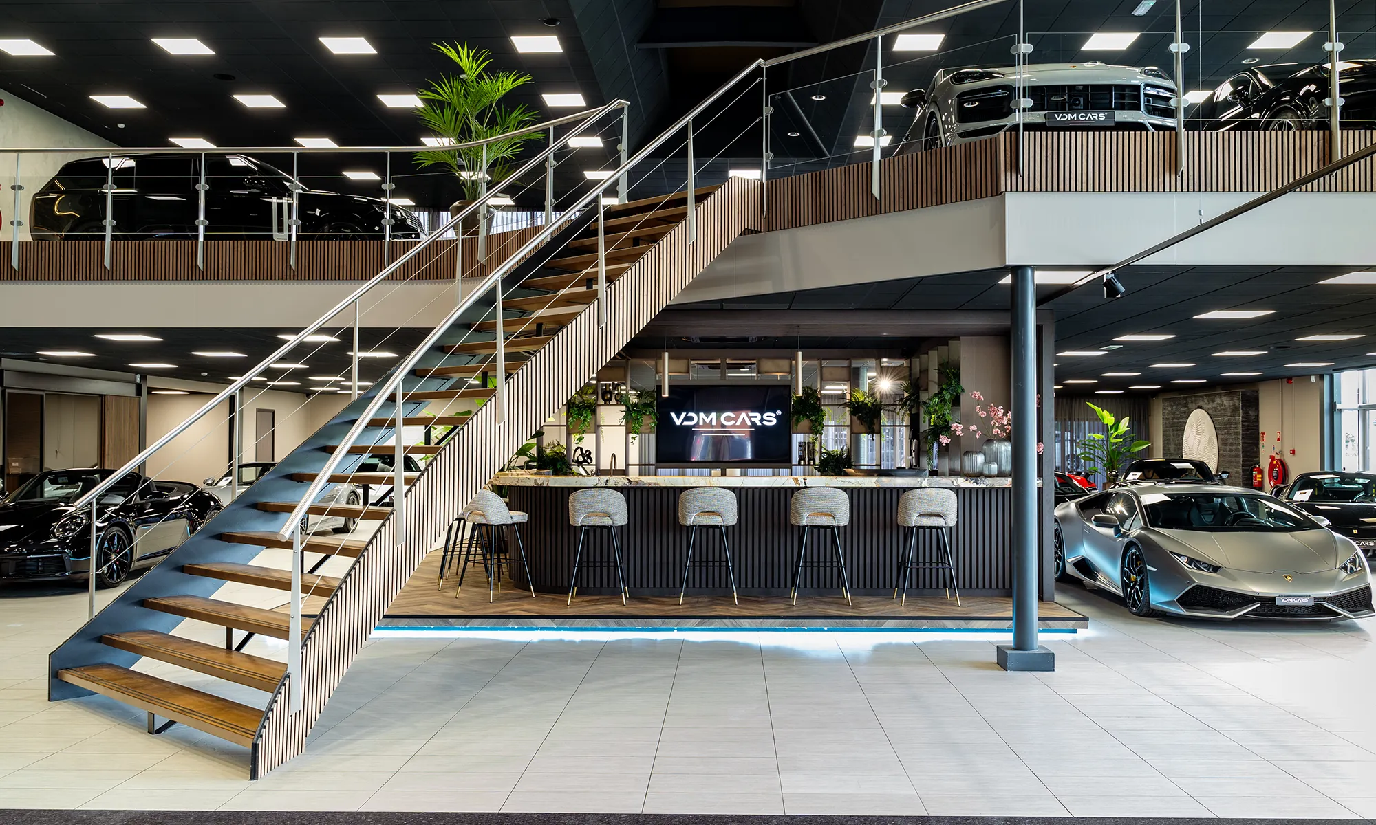 Moderne luxe autodealer showroom met trappen, bar en sportwagens van VDM Cars.