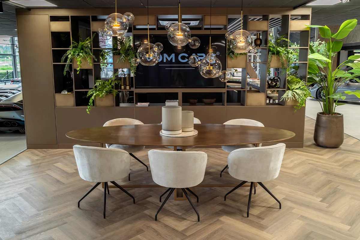 Moderne vergaderruimte met een ovale houten tafel, zes beige stoelen en hanglampen van glazen bollen.
