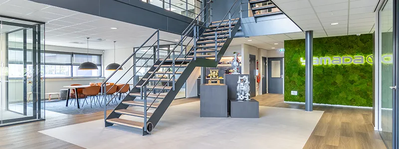 Modern kantoorruimte met open trap, vergadertafel en groene mosmuur.