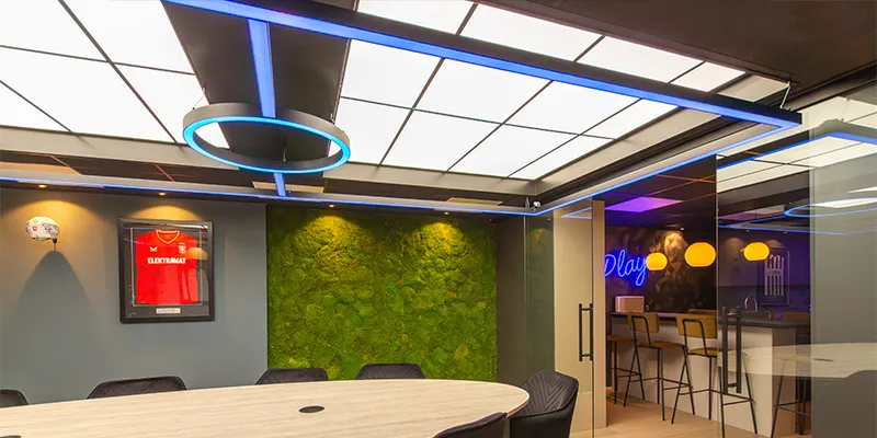 Moderne vergaderruimte met groene mosmuur, houten tafel en blauwe LED-verlichting.