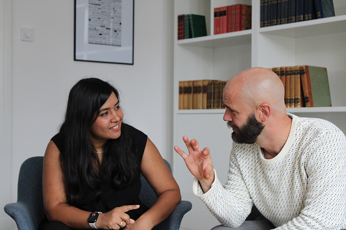 A woman and a man having an engaged conversation in a room with bookshelves behind them.
