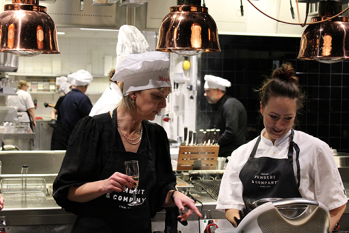 Two chefs in white hats and black aprons working together in a busy kitchen under copper lights.