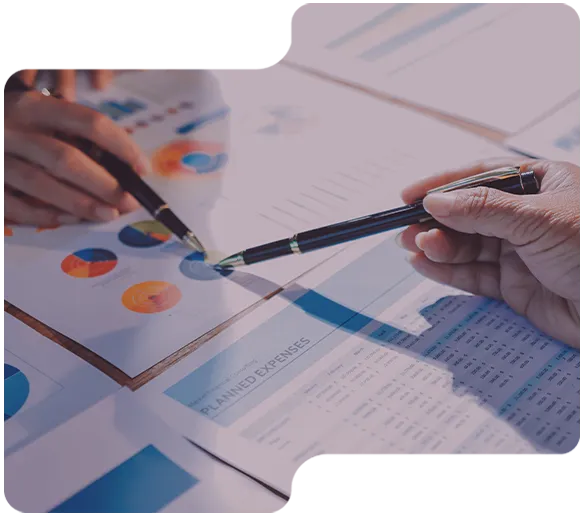 Two hands holding pens pointing at colorful pie charts and a planned expenses document on a table.