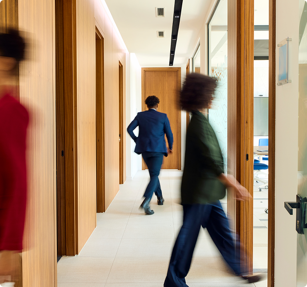 Blurred motion of three businesspeople walking in a modern office corridor with wooden doors.