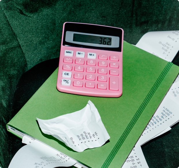 Pink calculator displaying 362 on a green notebook with crumpled and long receipts around it.