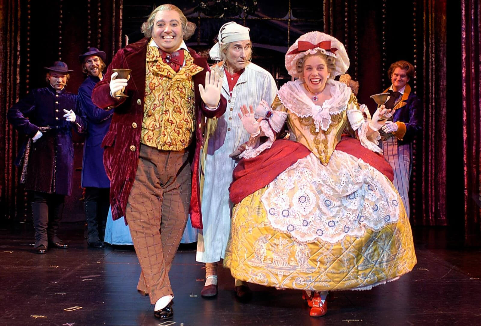 Roland Rusinek, Jim Dale and Kelly Ellenwood singing "Mr. Fezziwig's Annual Christmas Ball", with glasses and large, vibrant costumes