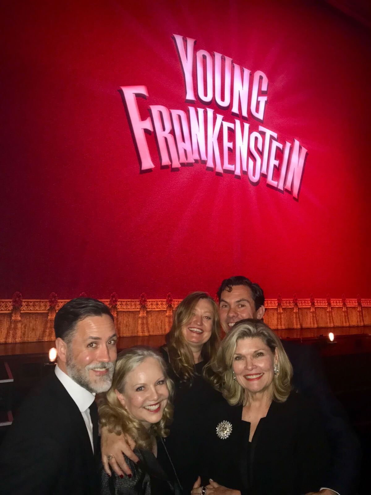 Susan Stroman and four associates in front of the red curtain showing "Young Frankenstein" in neon letters before the show starts on the West End.