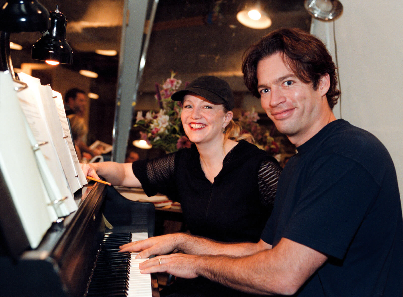 Susan Stroman and Harry Connick, Jr. sitting in a piano chair, working together.