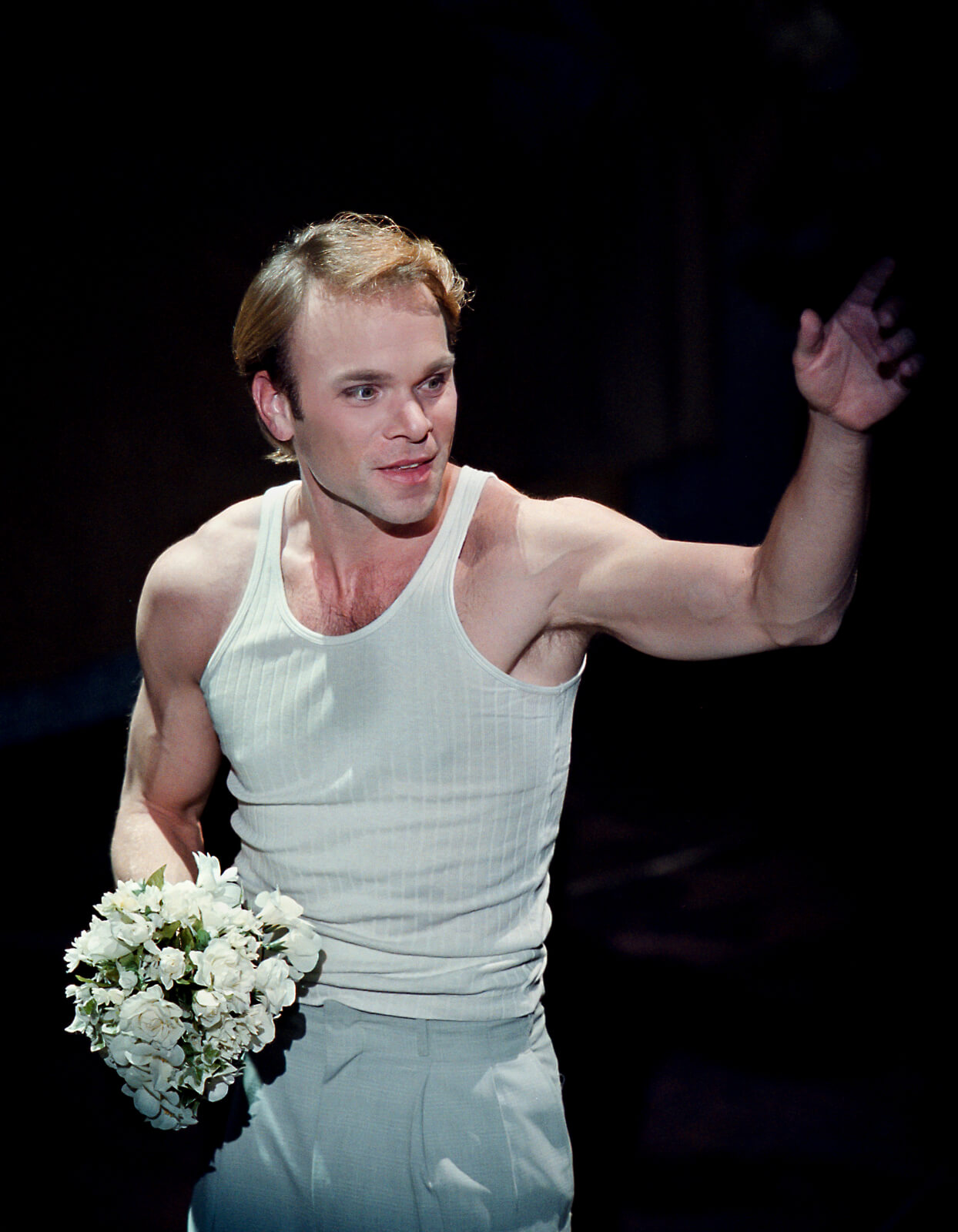 Camille Raquin (Norbert Leo Butz) in a white top, holding a small bouquet of white flowers