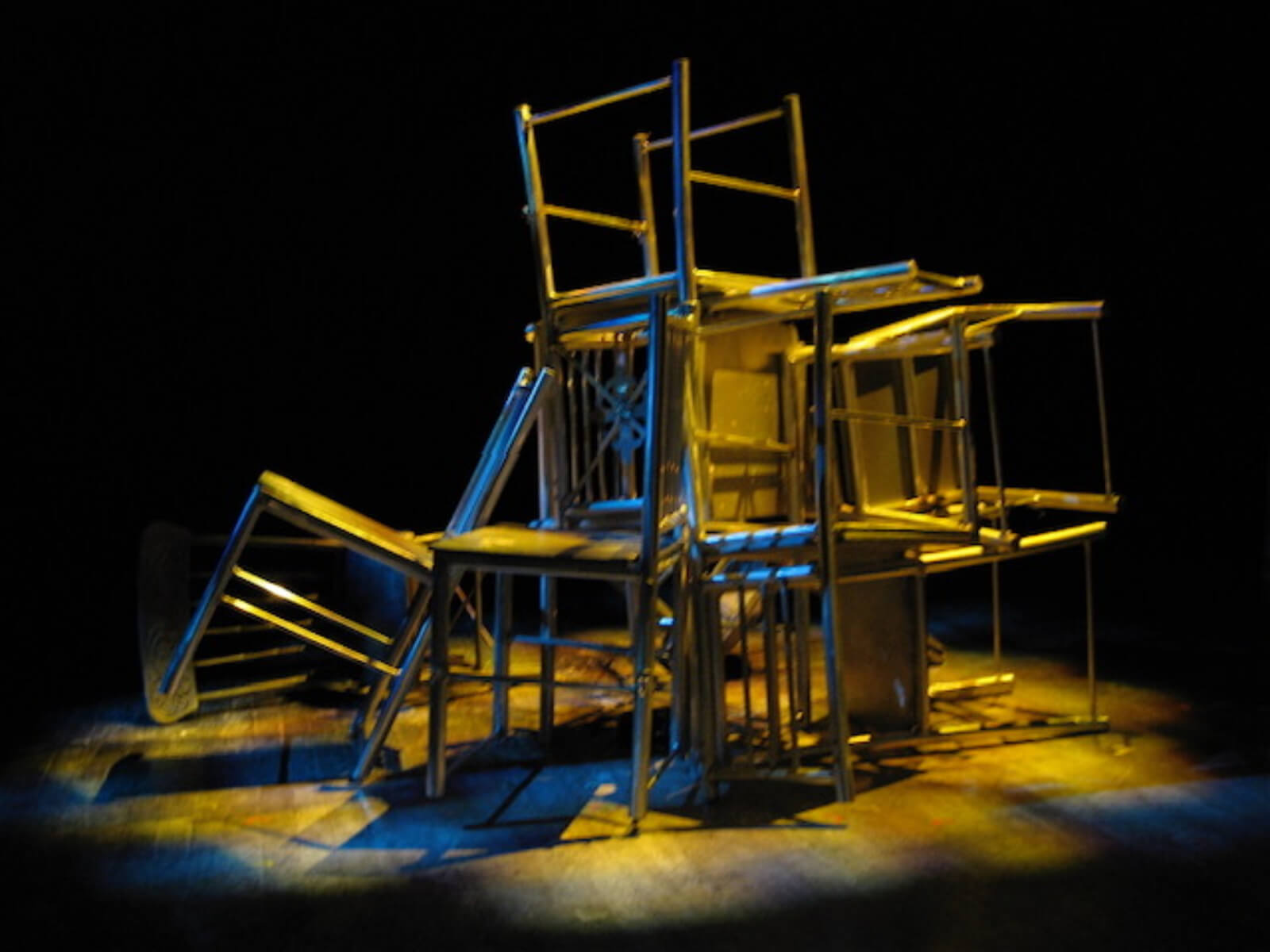 The lights are focused on a group of silver chairs, preset on the stage before the show opens. They are bathed in colored light. 
