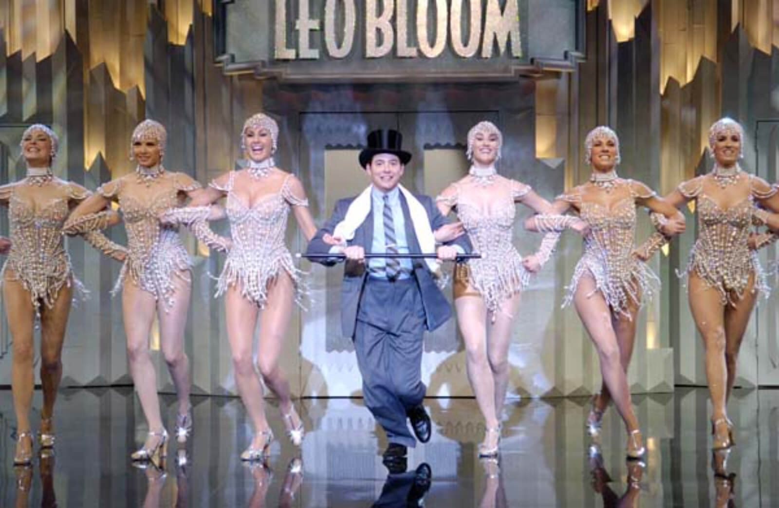 Leo Bloom (Matthew Broderick) and the Pearl Girls dancing "I Wanna Be a Producer". Leo dances with a top hat and cane. The girls are lined up on each side of him. 