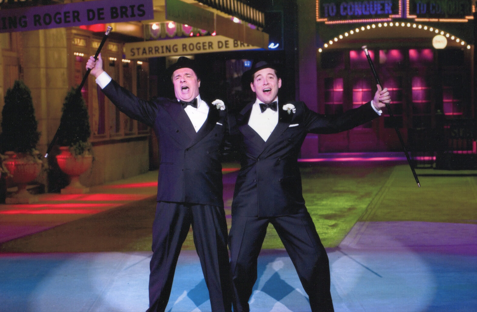 Max Bialystock (Nathan Lane) and Leo Bloom (Matthew Broderick) singing "Leo and Max". They are in Shubert Alley bathed in colored lights. They dance with fedoras and canes. 